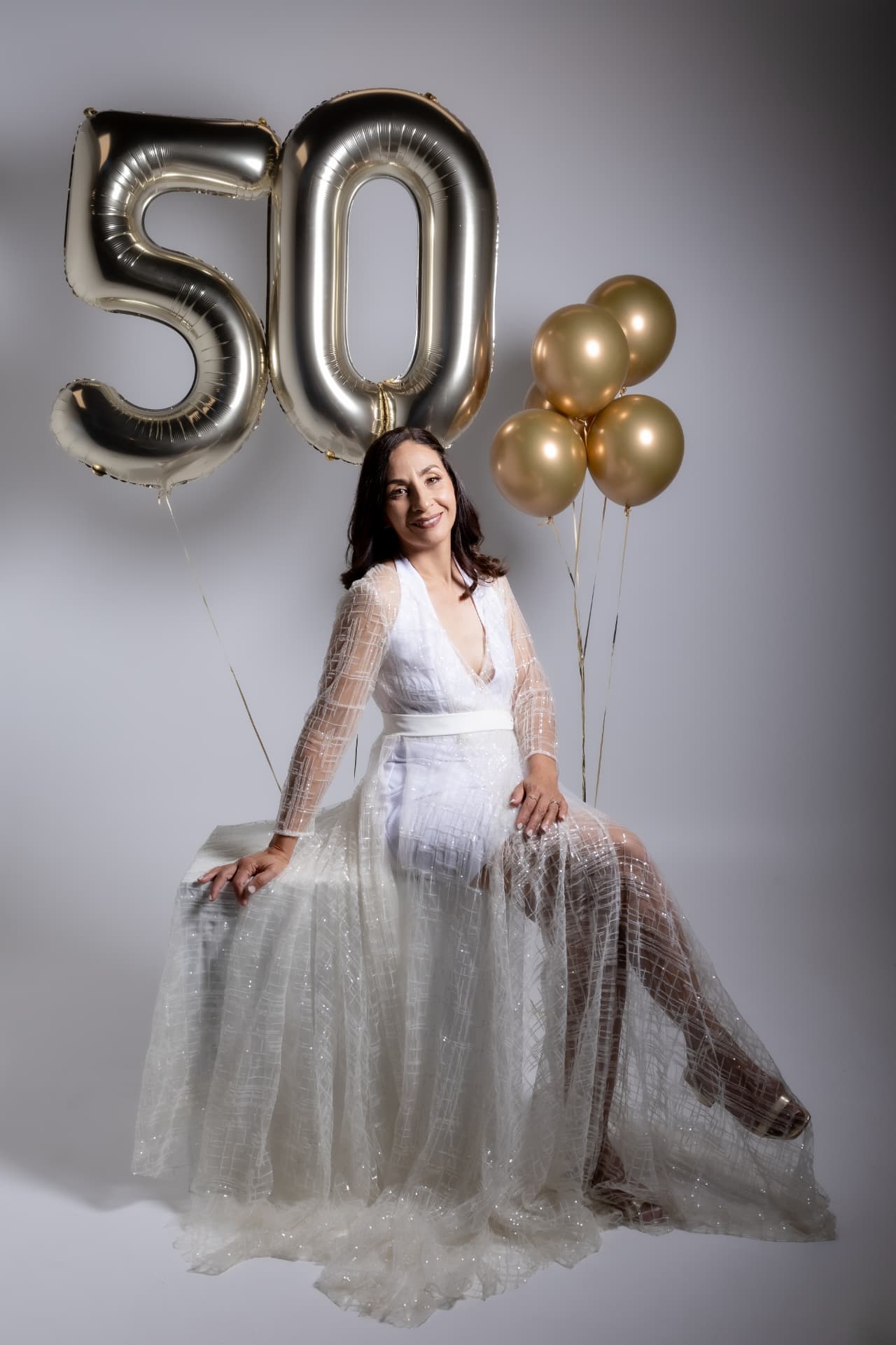 Mujer con vestido blanco y globos dorados celebrando 50 años