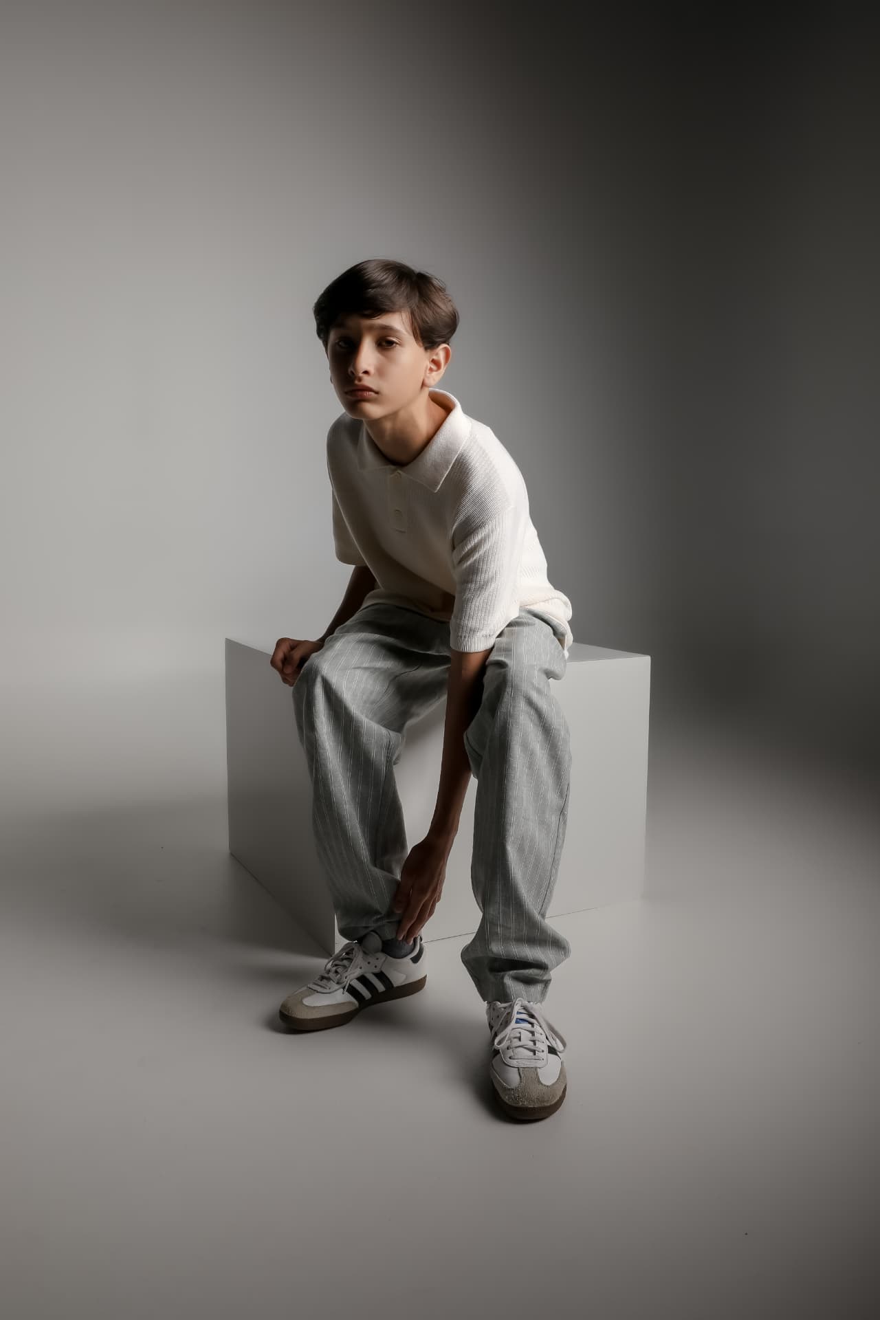 Retrato editorial de joven con camisa polo blanca sobre fondo gris