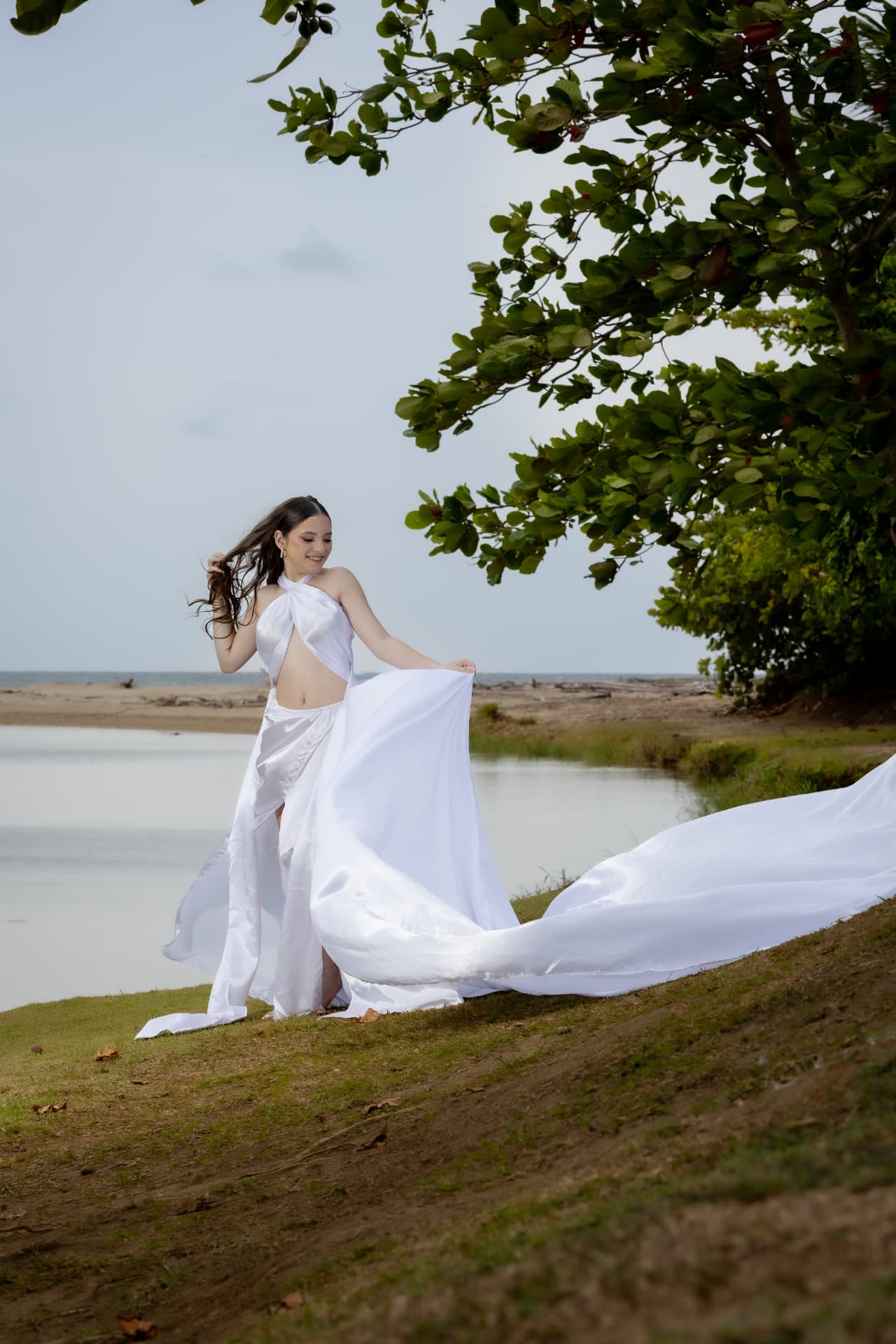 Joven en vestido blanco con tela fluyendo junto a la orilla
