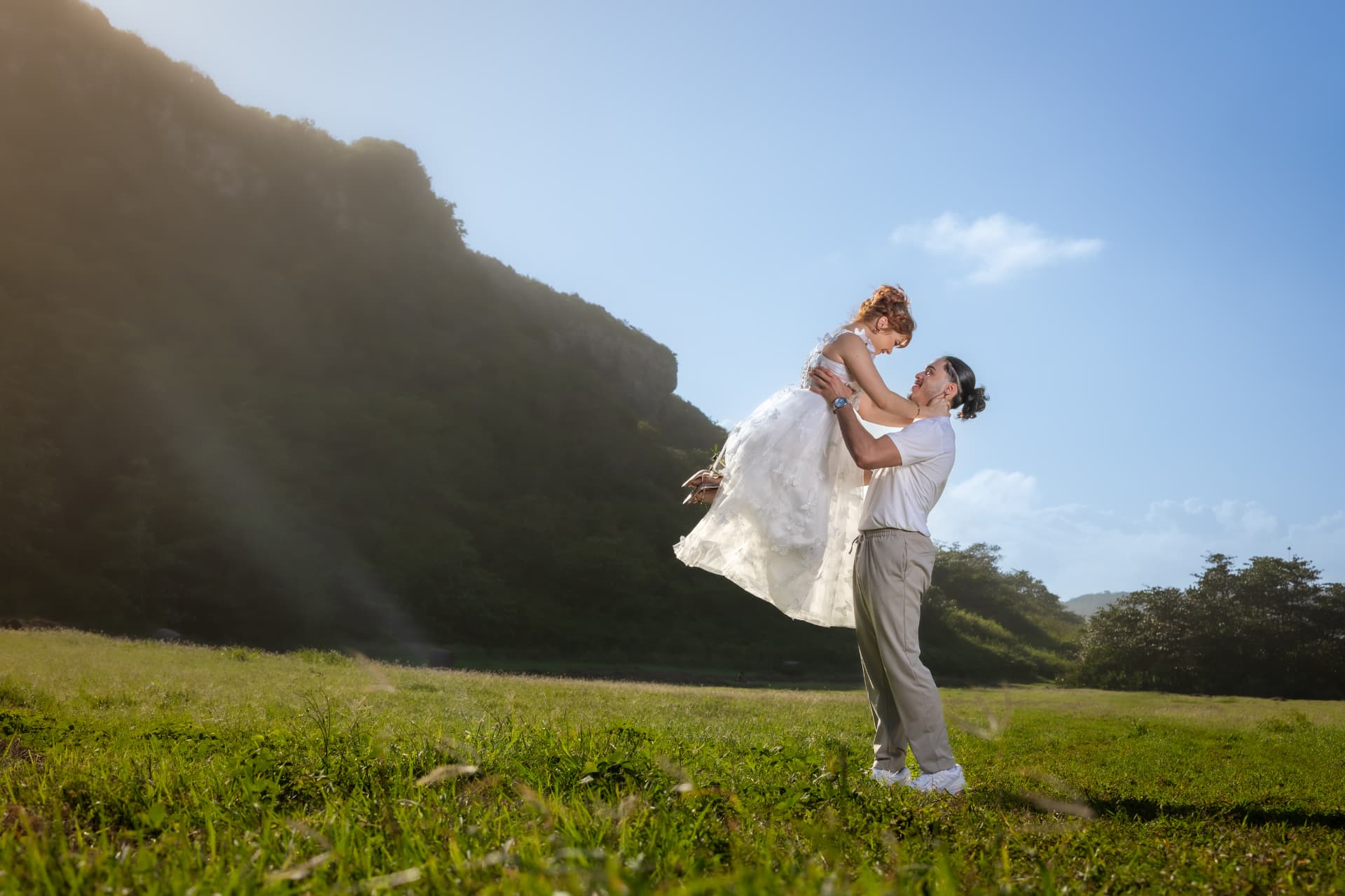 Pareja en campo verde con el hombre levantando a la mujer en vestido blanco
