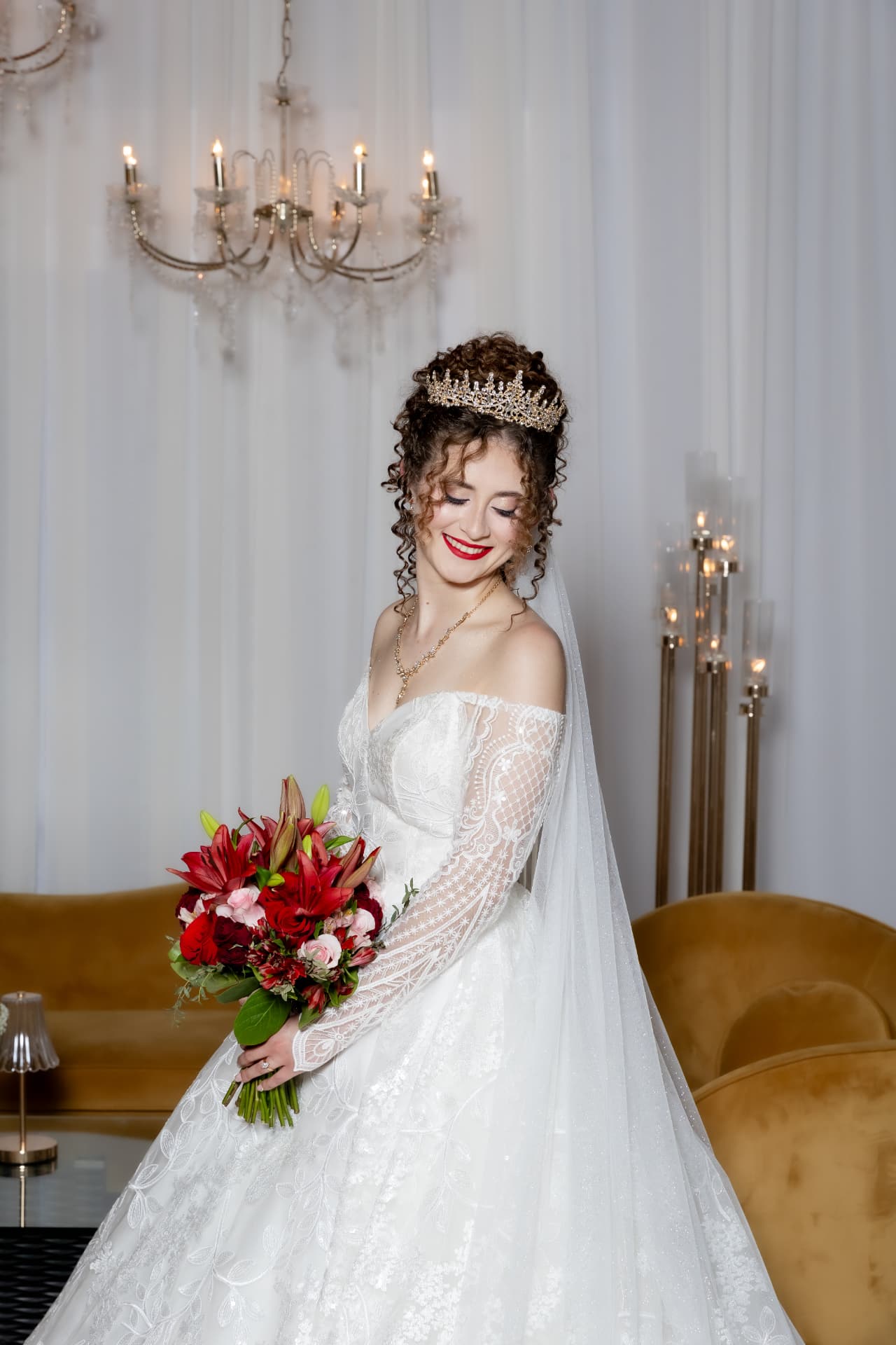 Novia sonriente con corona y bouquet rojo en elegante interior