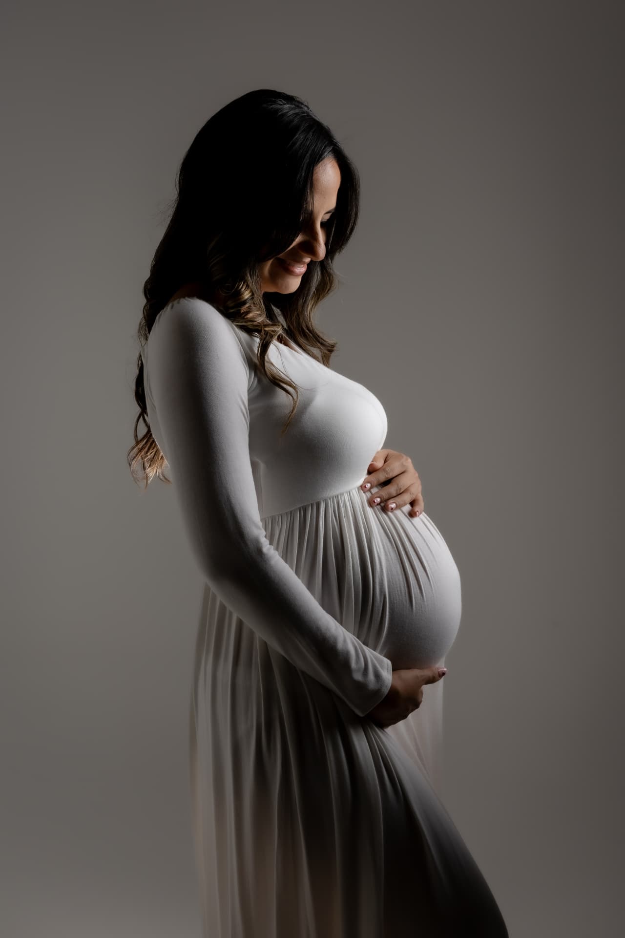Embarazada con vestido blanco de perfil sobre fondo oscuro