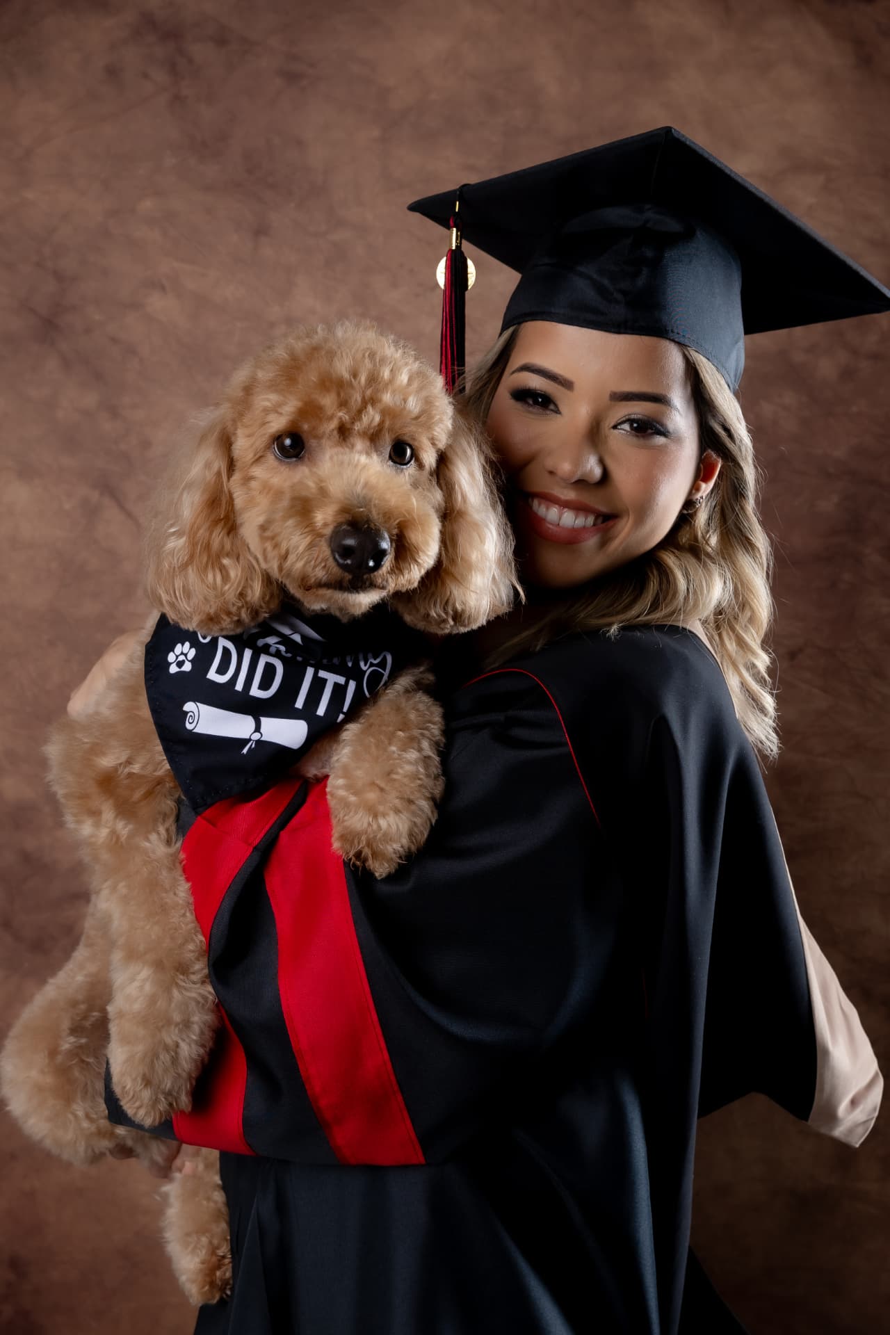 Graduanda sonriente sosteniendo a su perro durante su sesión