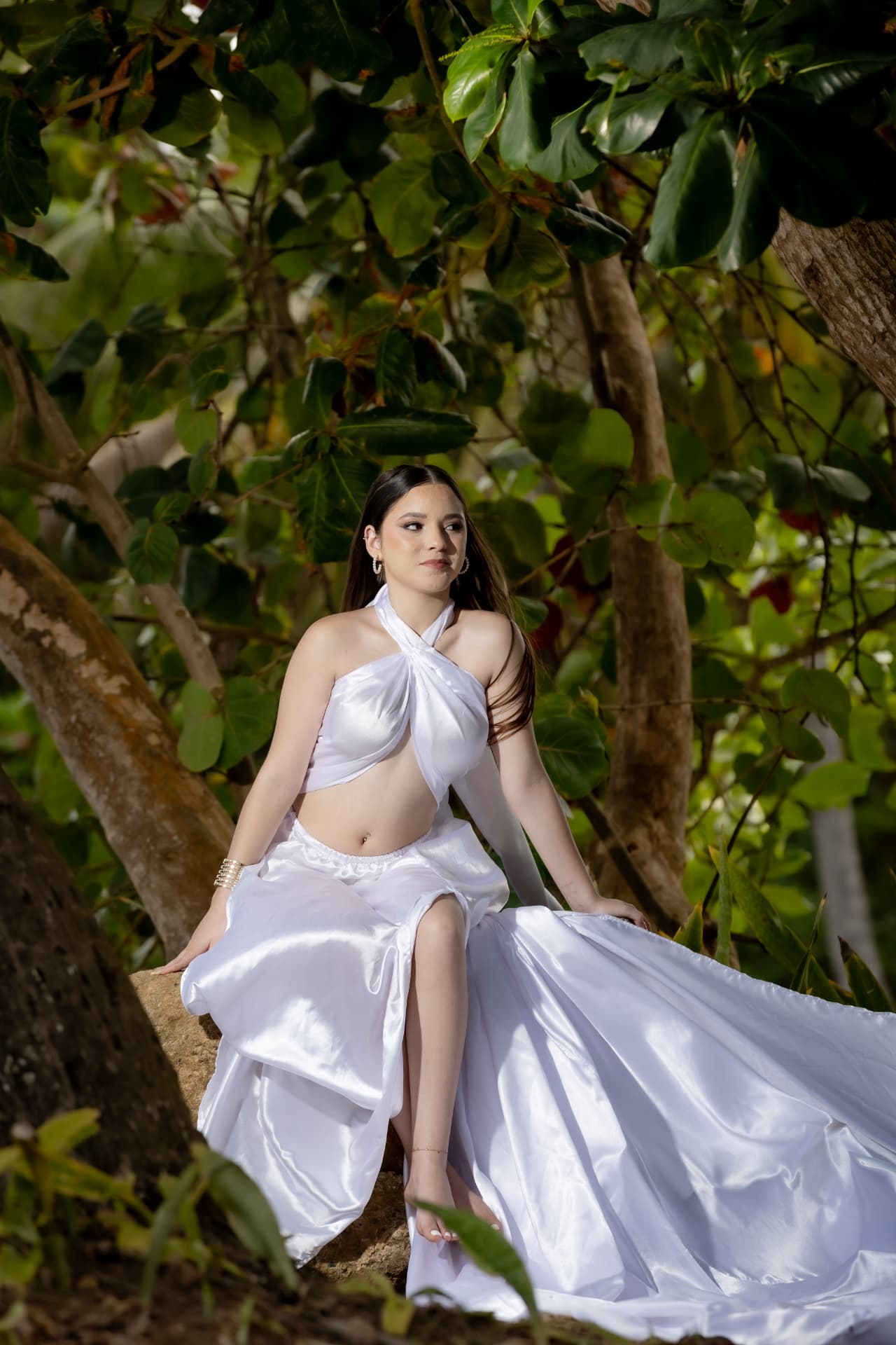 Joven en vestido blanco satinado entre árboles tropicales