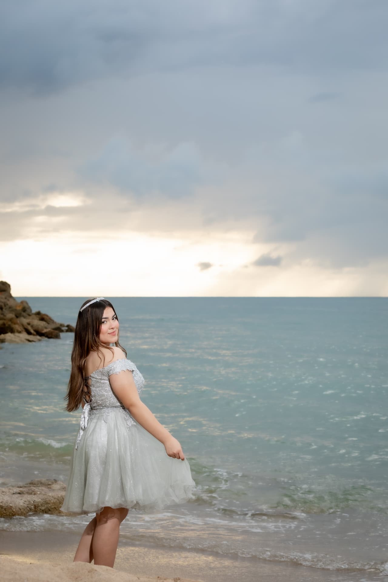 Joven en vestido corto plateado junto al mar al atardecer