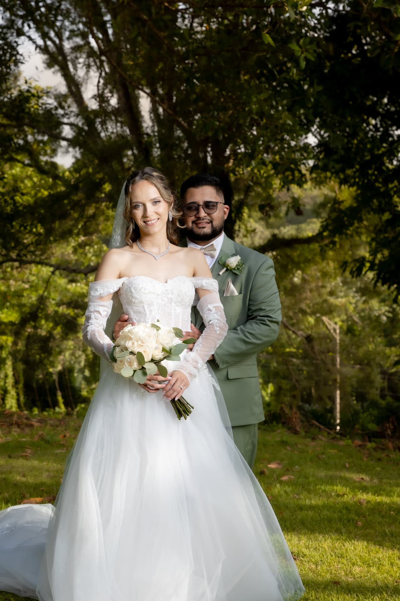 Novia con vestido blanco y novio con traje verde en jardín