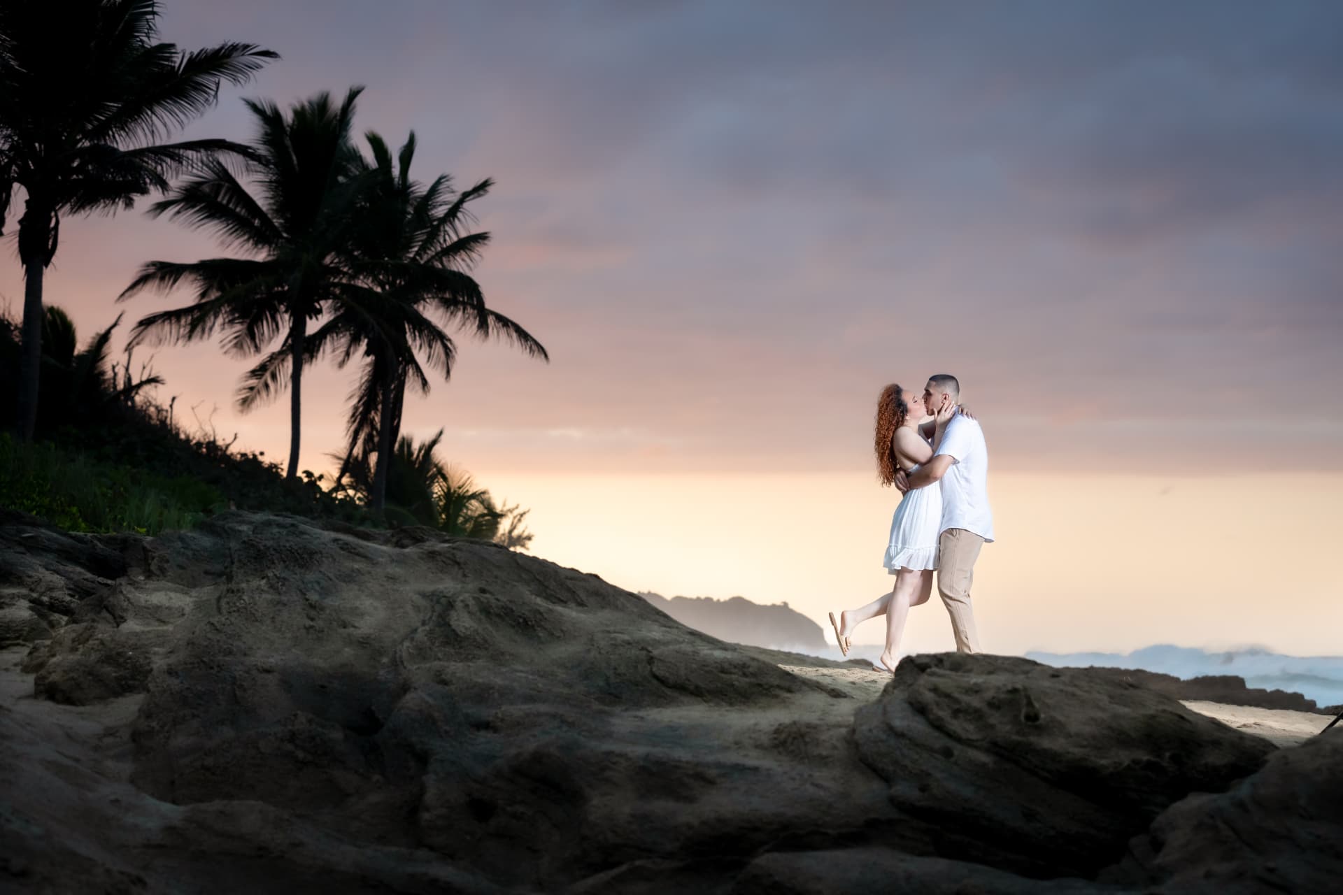 Pareja besándose al atardecer en la costa con palmeras
