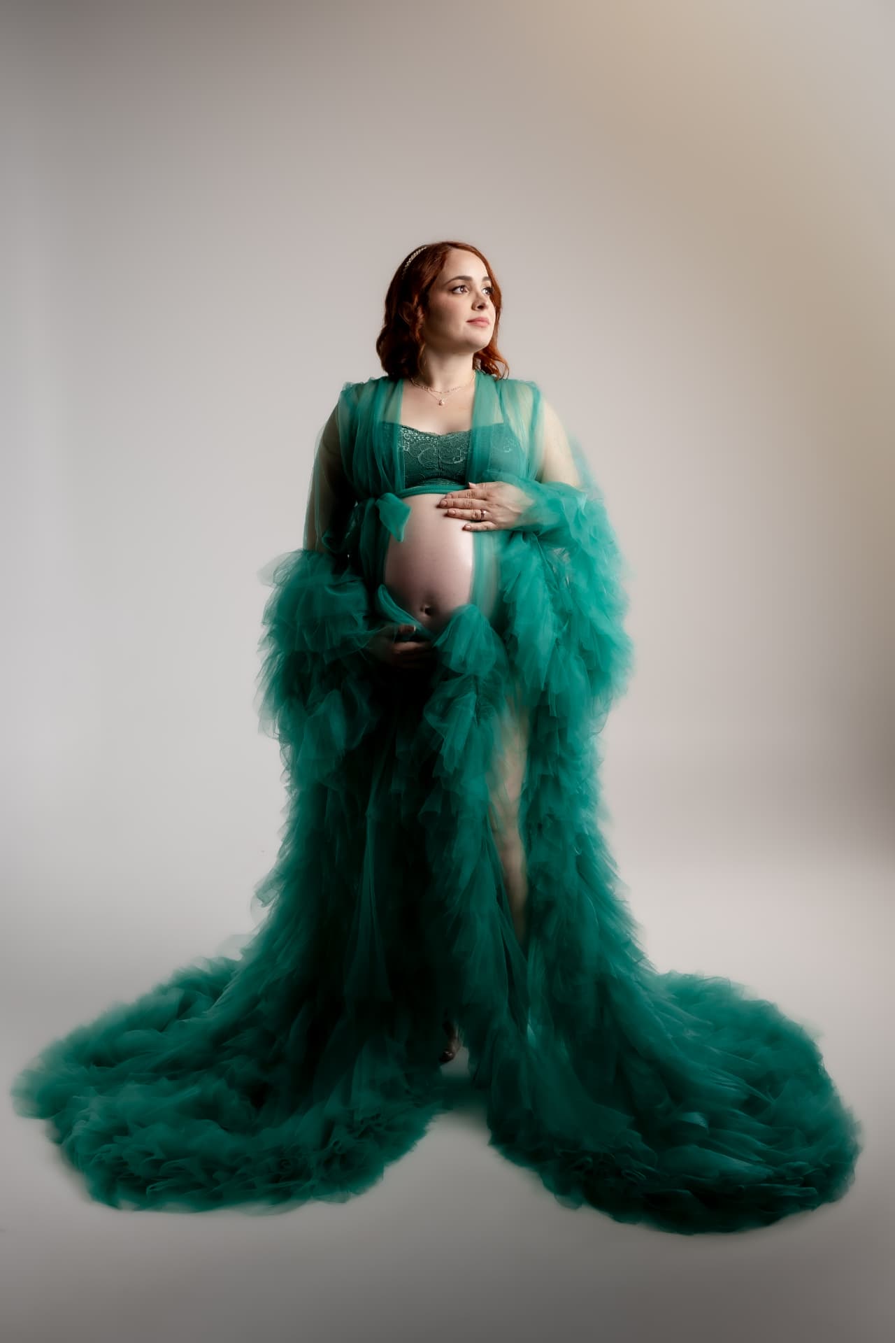 Embarazada con vestido verde de tul sobre fondo claro
