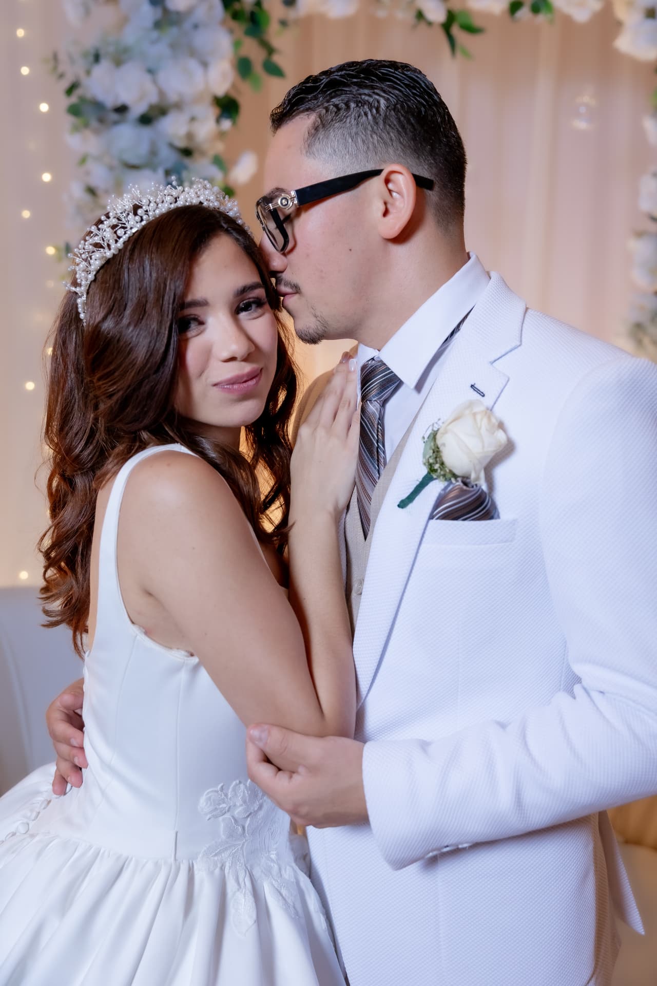 Pareja de novios abrazada en recepción con decoración floral y luces