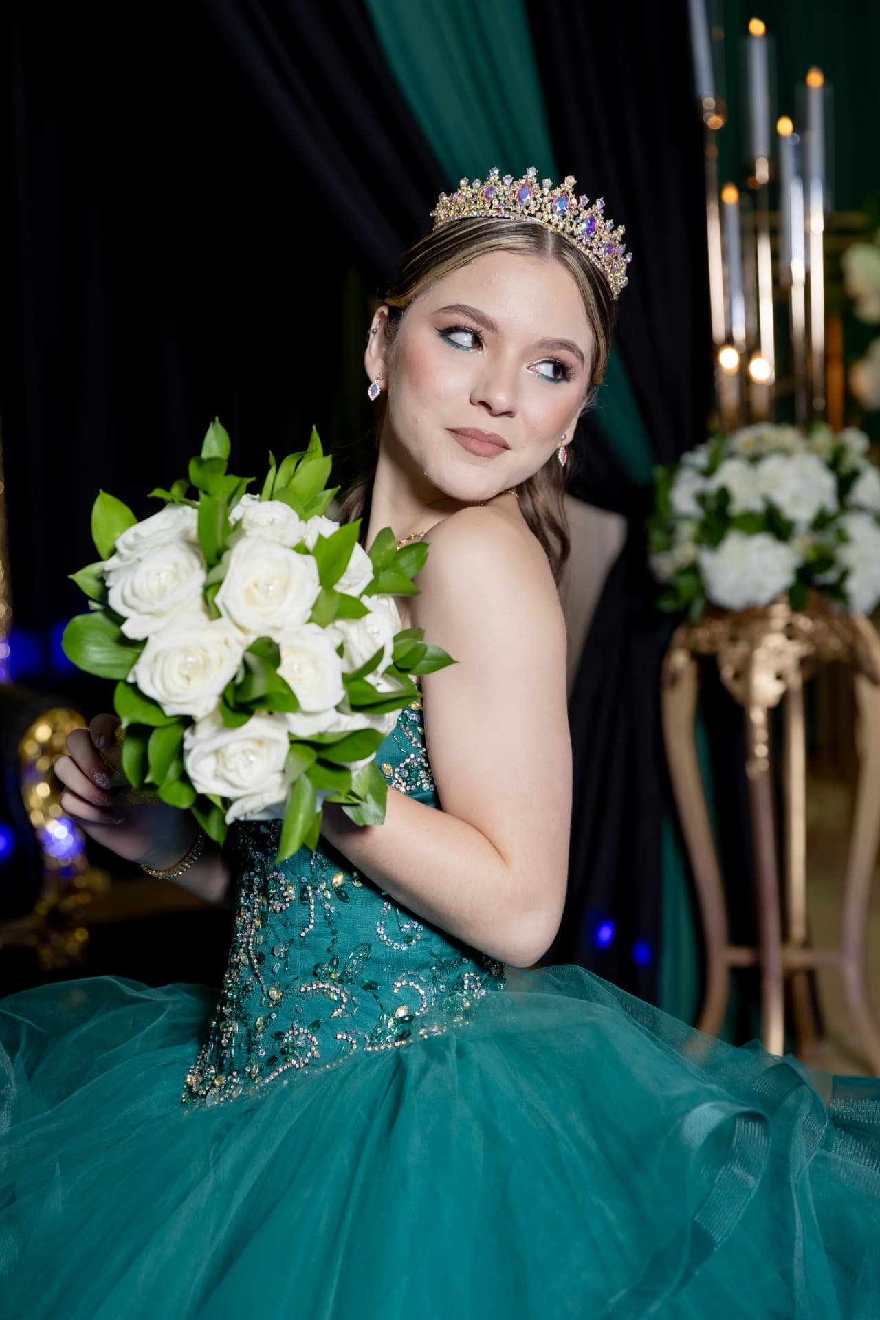 Quinceañera con vestido verde, corona y ramo de rosas blancas