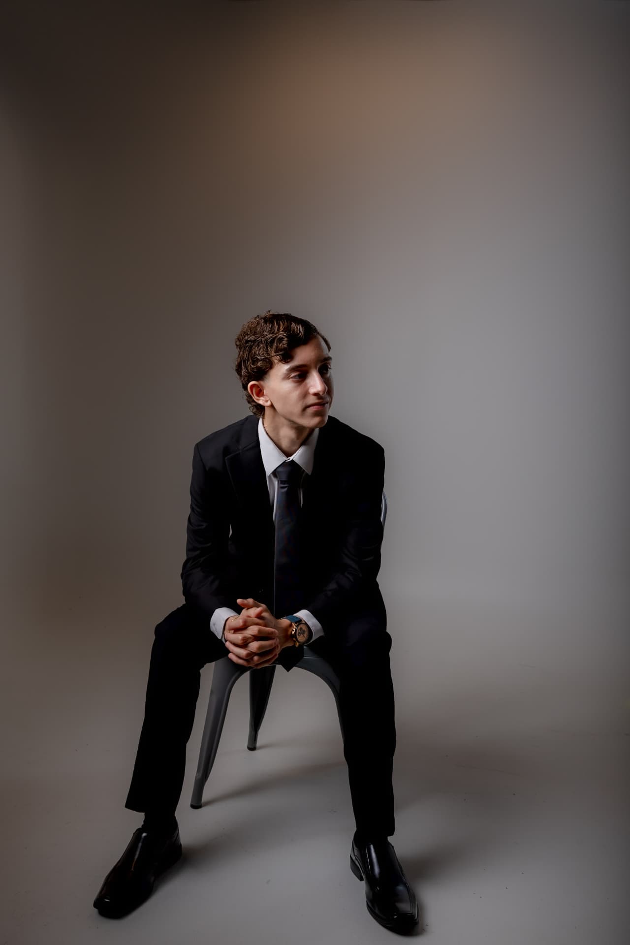 Retrato de joven con traje negro y corbata sentado en silla