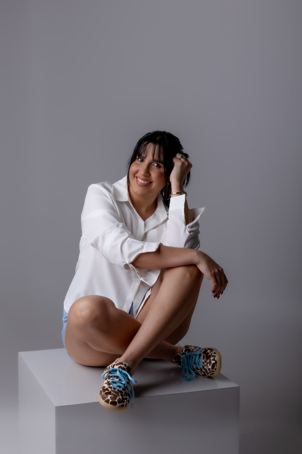 Retrato relajado de mujer con camisa blanca sentada en cubo blanco