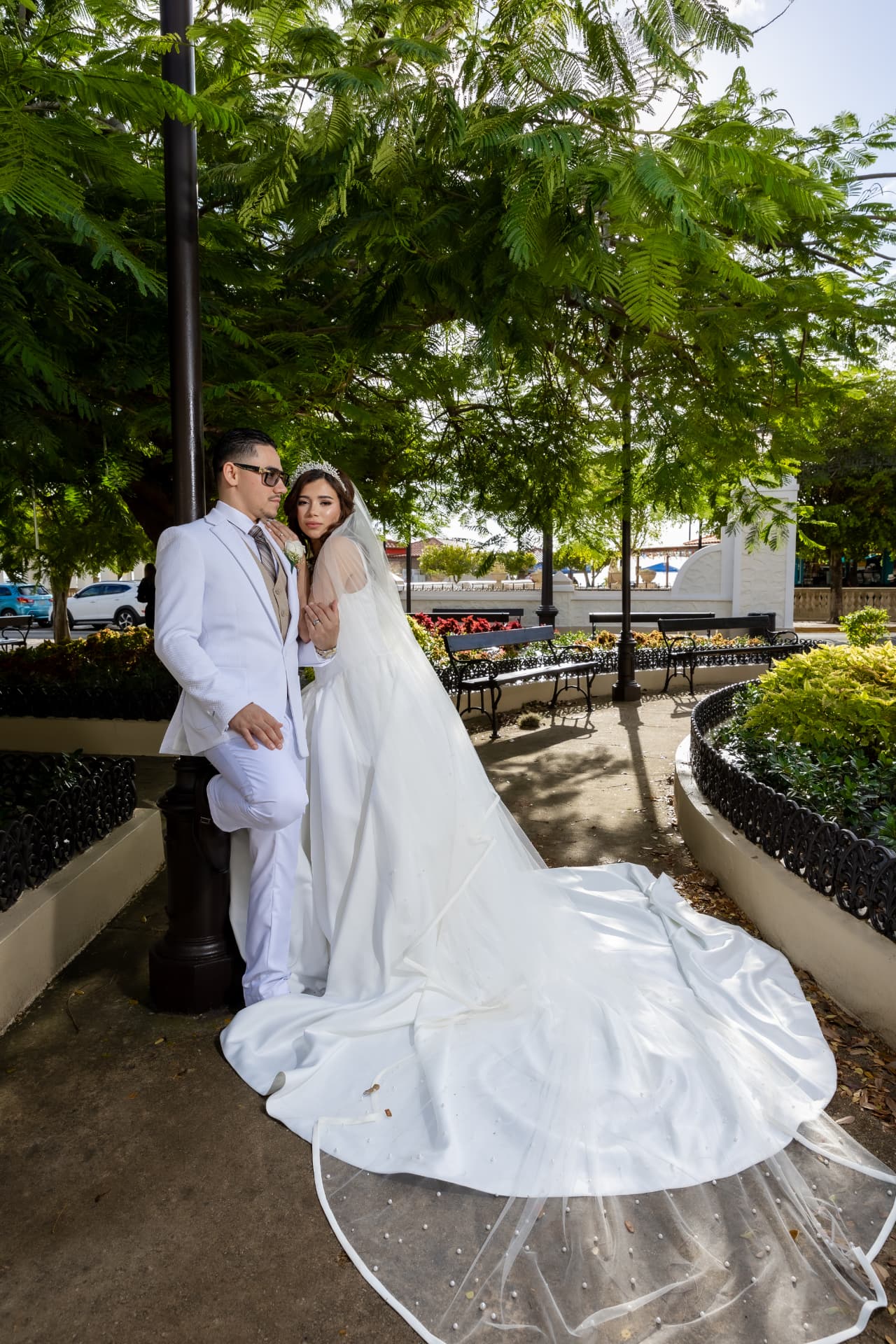Pareja de novios en jardín con vestimenta blanca y velo largo