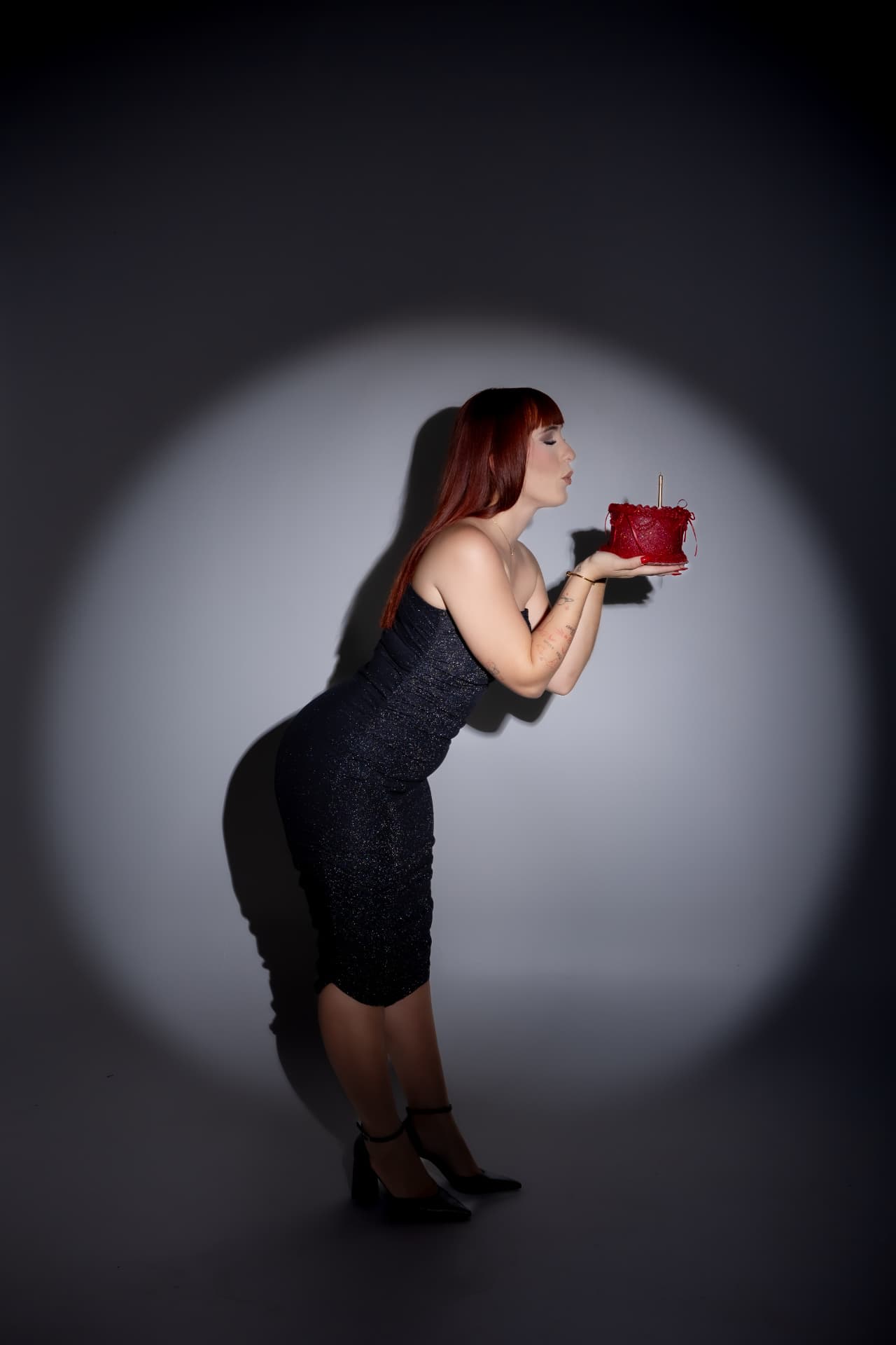 Mujer con vestido brillante soplando vela de pastel rojo