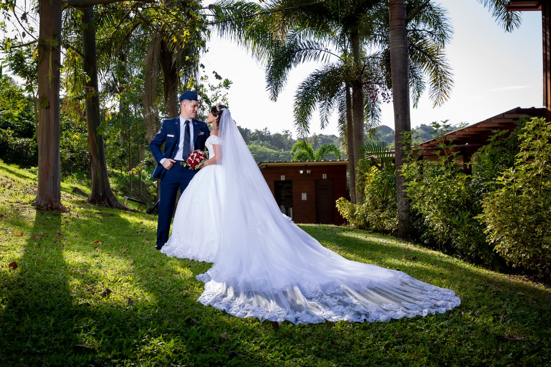 Pareja de novios en jardín con gran velo sobre el césped