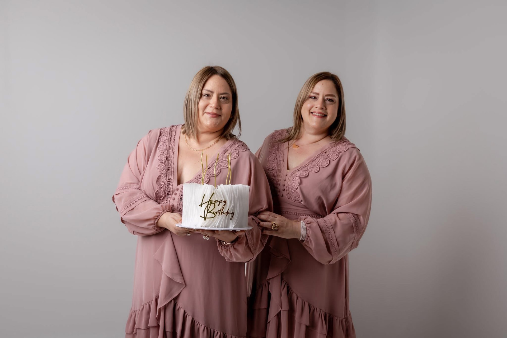 Dos mujeres con vestidos rosados sosteniendo pastel de cumpleaños