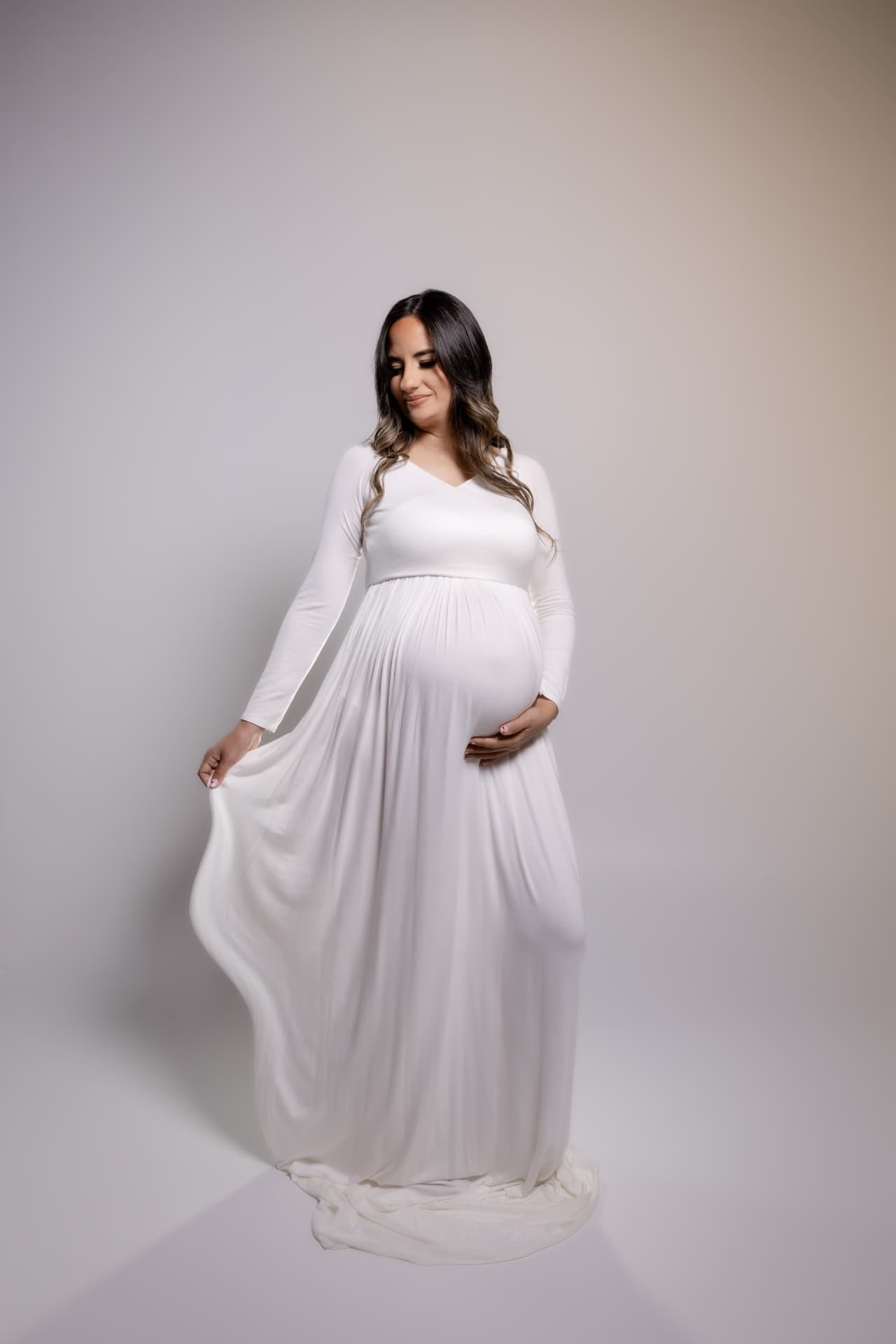 Embarazada con vestido blanco largo sobre fondo claro