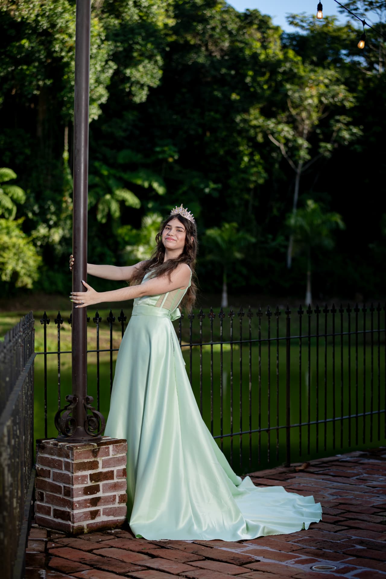 Joven en vestido verde menta con corona junto a verja de hierro