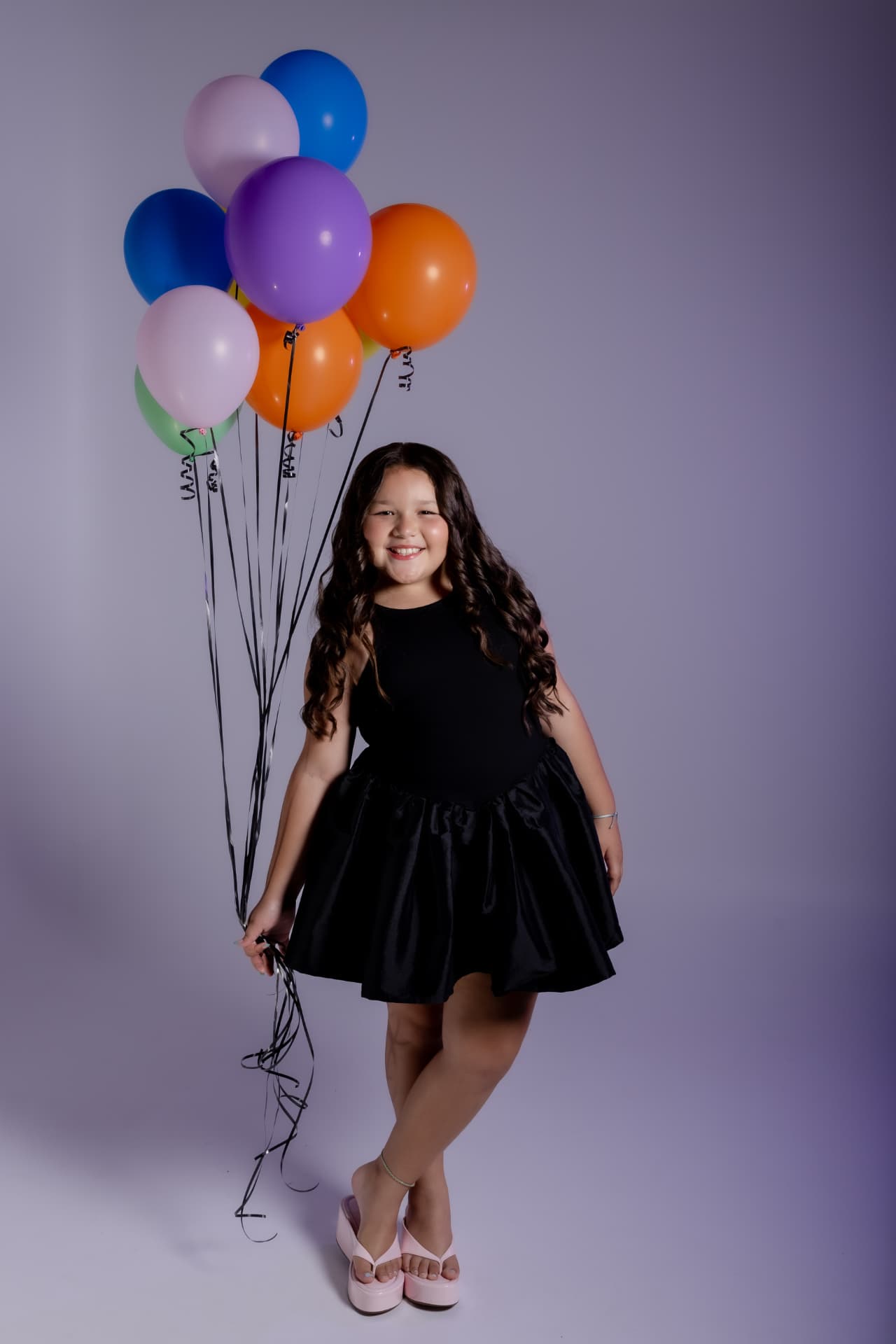 Niña sonriente con vestido negro y globos de colores