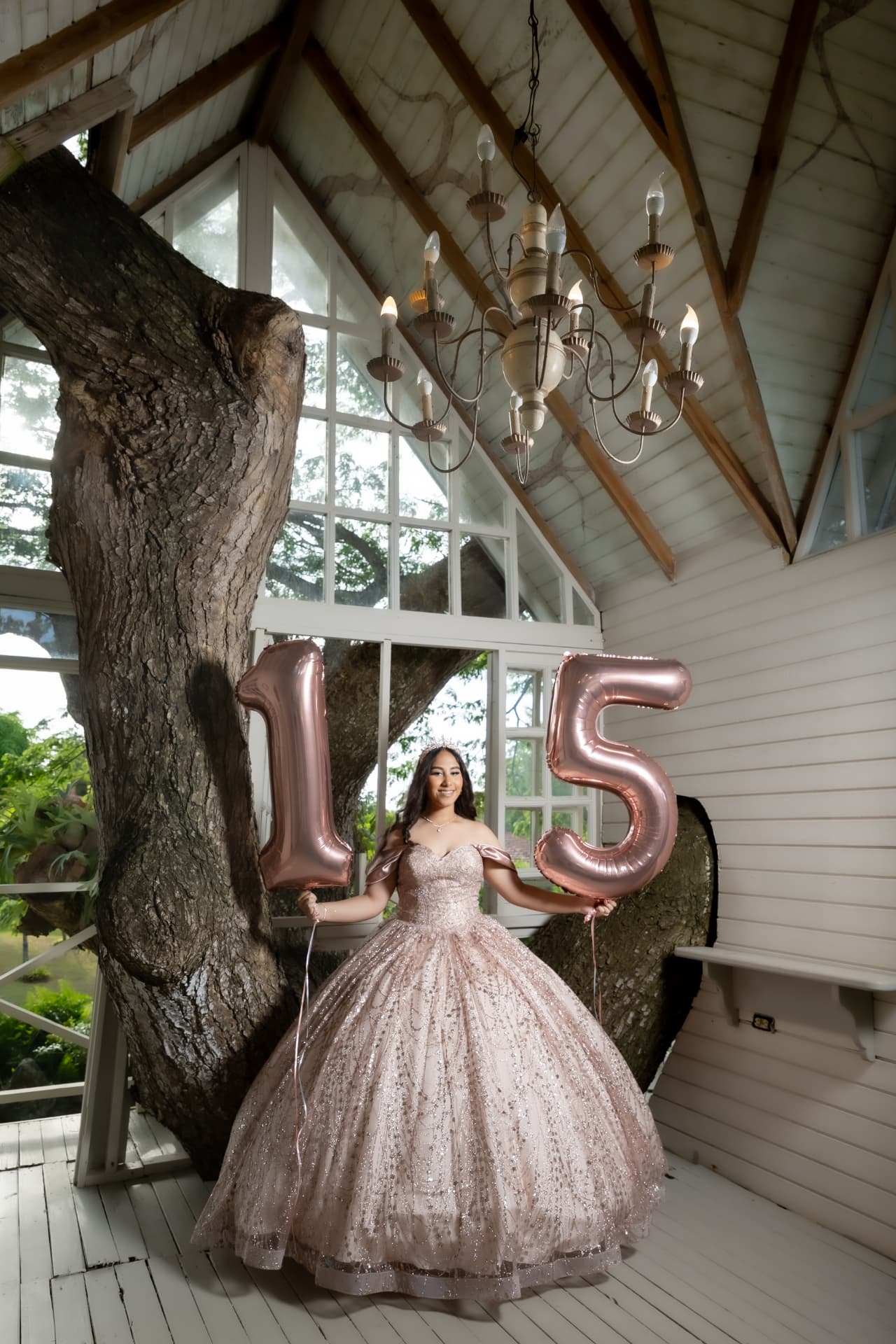 Quinceañera con vestido rosa y globos 15 en porche de madera