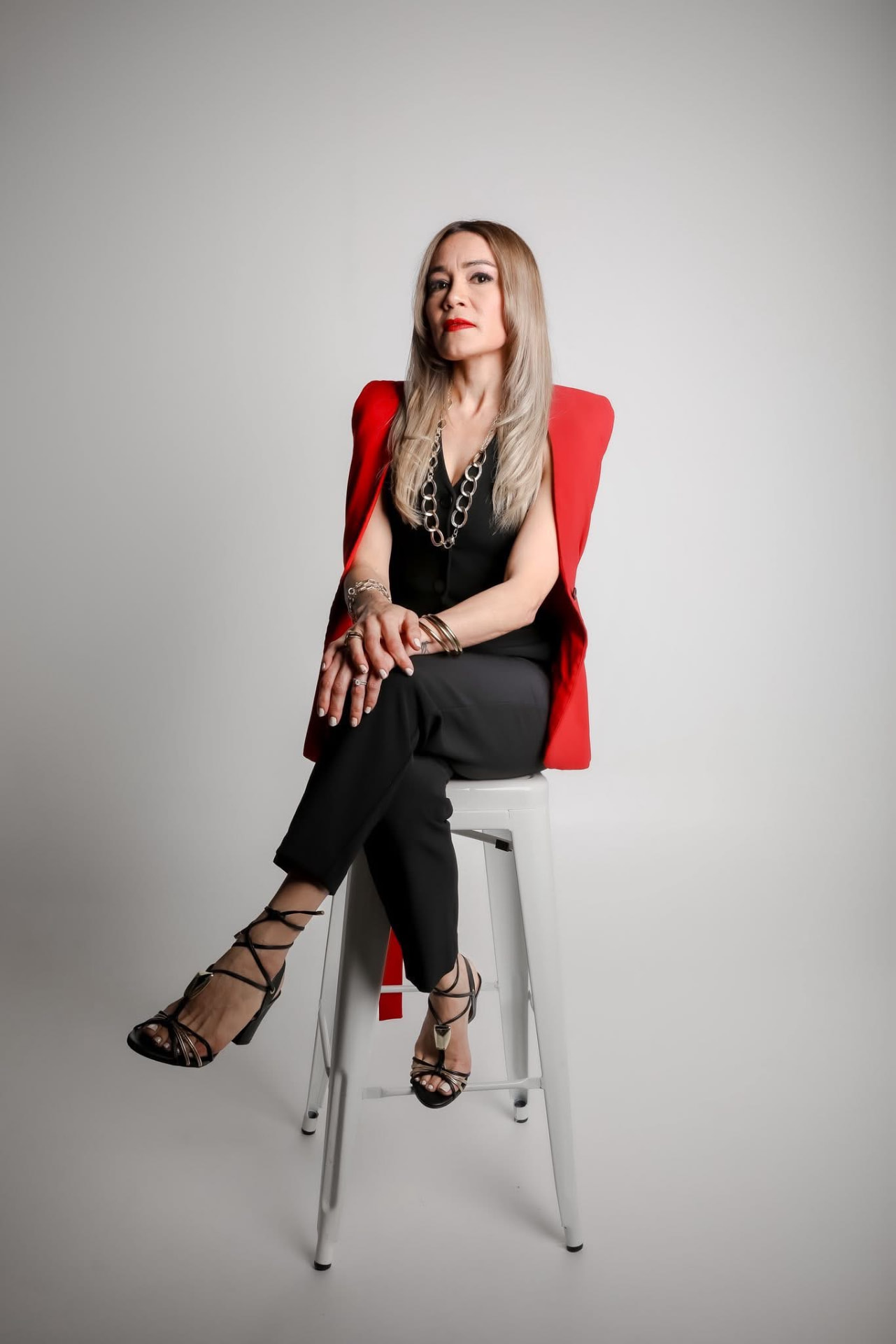Mujer con blazer rojo y vestido negro sentada en taburete