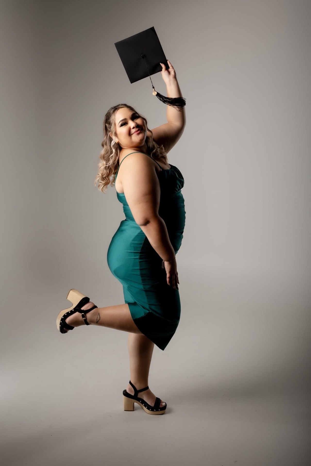Graduanda sonriente con vestido verde y birrete negro en studio