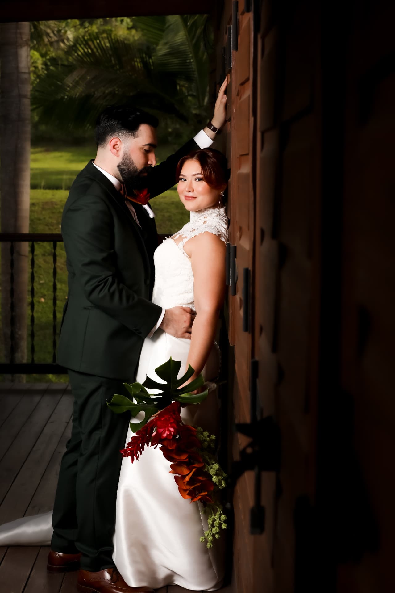 Novios posando junto a una puerta de madera con bouquet tropical